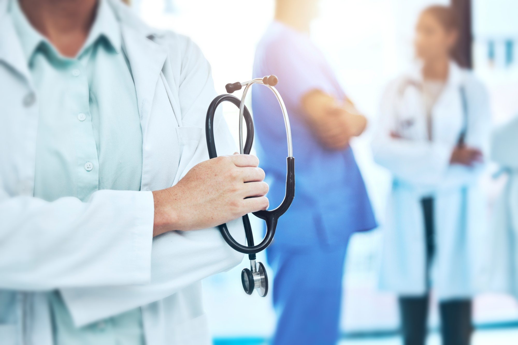 A doctor holding a stethoscope with colleagues behind